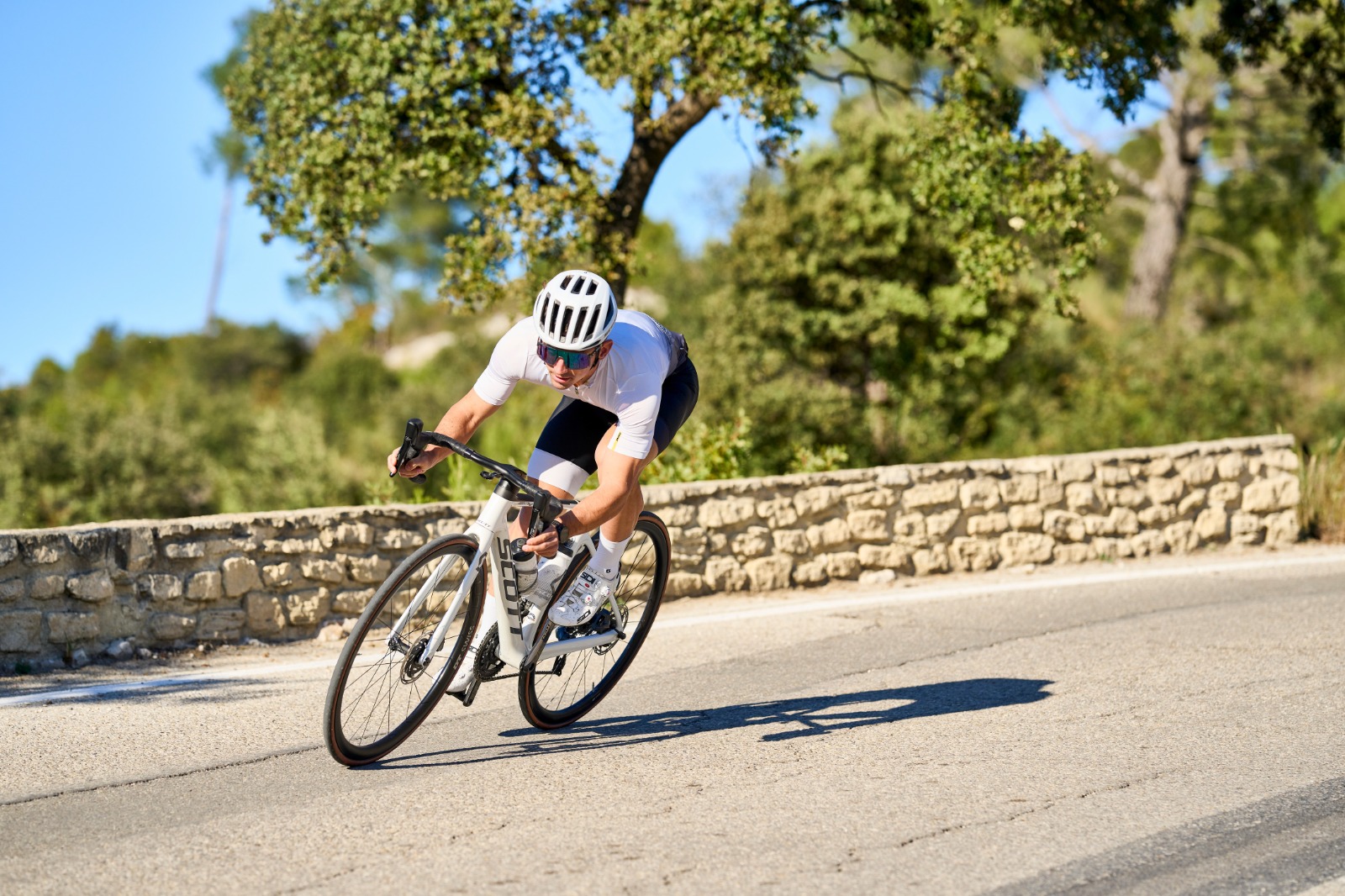 Road cyclist cornering on a sunny Provence road lined with a dry-stone wall
